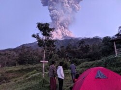 Beberapa wisatawan memperhatikan Gunung Merapi yang sedang erupsi, di Cangkringan, Sleman, Yogyakarta, 3 Maret 2020. (Foto: Antara via Reuters)