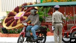 FILE PHOTO - A Cambodian police officer, right, talks with a motorcycle taxi driver next to a floral decoration set up ahead of the ASEAN Summit along a road in Phnom Penh, Cambodia, Sunday, April 1, 2012. 