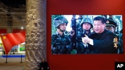 资料照片：2017年10月23日，一名男子在北京的一个视频屏幕旁边休息。视频显示，中国国家主席习近平在北京展览馆举行的一场展览上拿着一支步枪。（美联社照片）