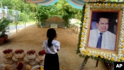 FILE - A girl stands by a portrait of Kem Ley, a Cambodian prominent political analyst, at his grave in Ang Takok, Cambodia, Nov. 20, 2016.