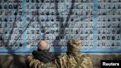 资料照：两名身穿迷彩服的男子在乌克兰基辅纪念墙前向在俄乌战争中牺牲的士兵致敬。（2023年3月14日）