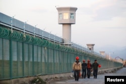 FILE - Workers walk by the perimeter fence of what is officially known as a vocational skills education center in Dabancheng, in Xinjiang Uighur Autonomous Region, China Sept. 4, 2018.