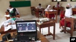 Siswa yang mengenakan masker duduk terpisah selama uji coba kelas dengan protokol COVID-19 di sebuah sekolah dasar di Jakarta, Jumat, 4 Juni 2021. (Foto: AP)