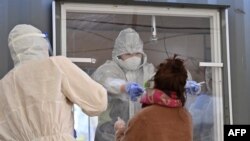 Seorang anggota staf medis yang mengenakan alat pelindung mengambil sampel dari seorang pengunjung untuk menguji virus corona di stasiun pengujian sementara di luar stasiun kereta api di Seoul pada 16 Desember 2020. (Foto: AFP)
