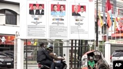 Seorang pengemudi becak menunggu pelanggan di depan poster pilpres 2024 di Medan, Sumatera Utara, 13 Februari 2024. (Foto: Binsar Bakkara/AP Photo)