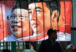 Seorang pria duduk di dekat spanduk Presiden Indonesia Joko Widodo dan wakilnya Ma'ruf Amin di Jakarta, Minggu, 20 Oktober 2019. (Foto: AP)