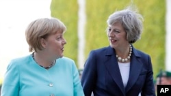 German Chancellor Angela Merkel, left, and British Prime Minister Theresa May walk on the red carpet during a military welcoming ceremony at the chancellery in Berlin Wednesday, July 20, 2016, on May's first foreign trip after being named British Prime Mi