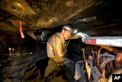 FILE - Scottie Stinson, a coal miner of 16 years, works to secure the roof with bolts in an underground coal mine roughly 40 inches high in Welch, West Virginia.