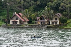 Seorang nelayan mendayung melewati hotel-hotel resor di pulau Samosir, Danau Toba, 3 April 2019. (Foto: dok).