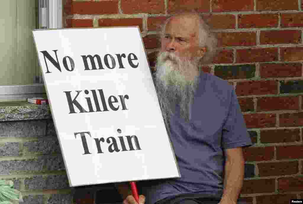 A man sits with a sign outside the school sheltering evacuees in Lac-Megantic, Quebec, Canada, July 10, 2013.