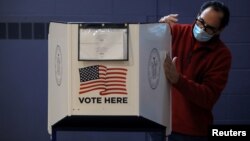Seorang petugas membersihkan bilik suara untuk mencegah penyebara virus corona (Covid-19) di tempat pemungutan suara (TPS) di Staten Island, yang buka untuk pencoblosan dini, New York, Minggu, 25 Oktober 2020. (Foto: Reuters)