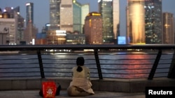FILE - A woman sits on the bank of the Huangpu River in Shanghai and looks out at the Pudong financial district, Sept. 27, 2024.