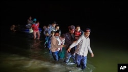 FILE - Migrant families, mostly from Central American countries, wade through shallow waters after being delivered by smugglers on small inflatable rafts on U.S. soil in Roma, Texas, March 24, 2021.