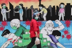 Seorang pegawai berjalan melewati mural bertema virus corona untuk menghormati tenaga kesehatan di RSUD Cengkareng Jakarta, Kamis, 24 Juni 2021. (Foto: AP)