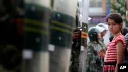 2009年7.5事件后，乌鲁木齐的一名维吾尔族女孩注视着一排中国防暴警察。（2009年7月9日）