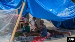 A woman and kids rest in the shade at a camp for people who lost their home during the August 14 earthquake in Les Cayes, Haiti, on August 23, 2021.