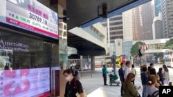 行人走过香港一家银行外的港股指数电子显示屏。