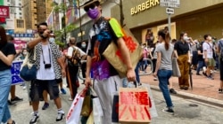 香港异见艺术家黄国才2020年7月1日，香港国安法实施第一日，在铜锣湾以”血拼”为名，打扮成来自中国大陆的”豪客”，手持多个写上国安法相关罪名的百货公司购物袋，表现对实施国安法的不安 （美国之音/汤惠芸）