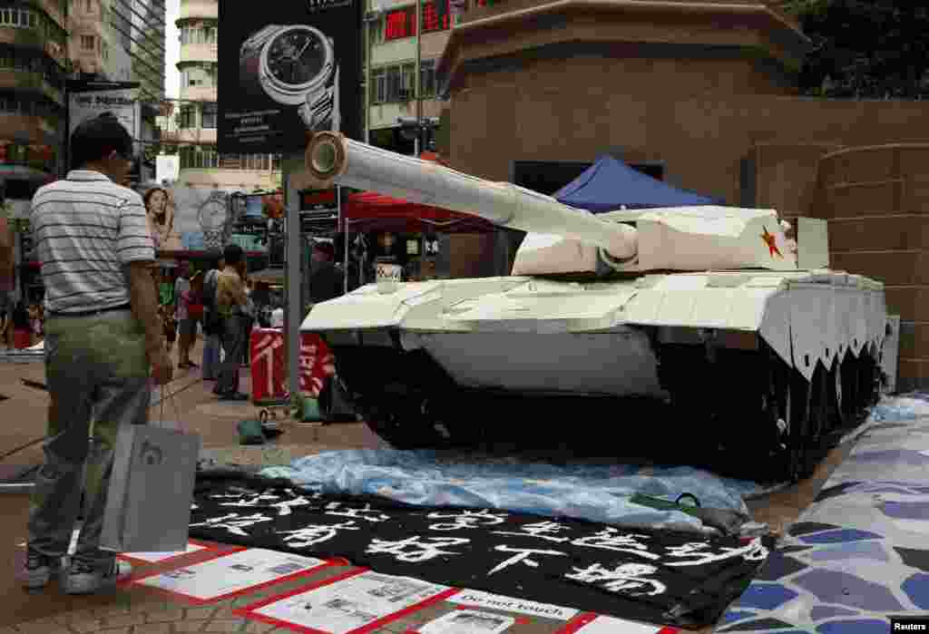 A shopper in Hong Kong stands in front of a model tank made by university students to remember the crackdown in Tiananmen Square, June 3, 2014.