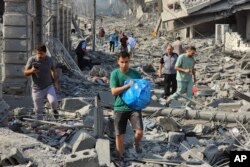 Warga Palestina berjalan melewati puing-puing bangunan yang hancur akibat serangan udara Israel di Kota Gaza pada Selasa, 10 Oktober 2023. (Foto: AP)