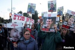 Seorang perempuan memegang foto sandera Israel Yagev Buchshtab, sementara orang lain mengangkat foto sandera lainnya dalam sebuah protes di Yerusalem pada 9 April 2024, menuntut kesepakatan dan pembebasan sandera yang ditahan di Gaza. (Foto: Reuters)