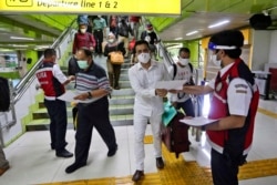 Para petugas membagikan masker kepada para penumpang di Stasiun Gambir untuk mencegah penularan virus corona.