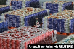 Seorang pekerja memakai masker pelindung saat menyusun tumpukan karung berisi beras, di tengah wabah Covid-19 di Surabaya, Jawa Timur, 20 April 2020. (Foto: Antara/Moch Asim via REUTERS)