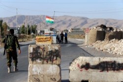 FILE - Kurdish Peshmerga fighters man a checkpoint as words written on stone slabs by the Islamic State are seen painted out, at Makhmur town, Sept. 10, 2014.