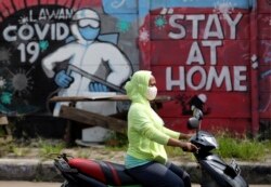 Seorang perempuan mengenakan masker mengendarai sepeda motornya melewati mural bertema Covid-19 selama pandemi corona di pinggiran Jakarta, 2 Juni 2020.