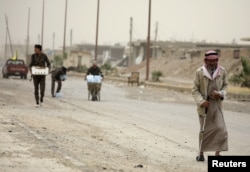 A civilian and fighters from the Syrian Democratic Forces (SDF) walk along a street in the Raqqa's al-Sana'a industrial neighborhood, Syria June 14, 2017. Mutual suspicion between Arabs and Kurds in Raqqa runs deep and predates the current conflict by decades.