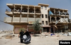 A member of the Iraqi security forces holds an Islamic State flag, after pulling it down from a building, in Fallujah, Iraq, June 25, 2016.