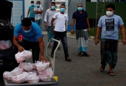 Para pekerja migran yang tinggal di asrama milik pabrik mengambil makanan yang didonasikan oleh sejumlah badan amal untuk Idul Fitri di tengah wabah virus corona di Singapura, 24 Mei 2020. (Foto: Reuters)