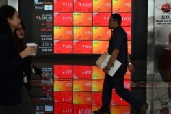 Para pengunjung melintas di depan layar yang menunjukkan data perdagangan Bursa Efek Indonesia (IDX), di Jakarta, 9 Maret 2020. (Foto: AFP)