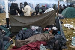 FILE - A migrant man sleeps in a camp near Bruzgi-Kuznica checkpoint on the Belarusian-Polish border in the Grodno region, Belarus, Nov. 18, 2021.