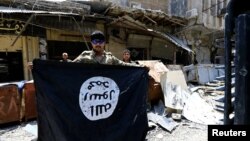 FILE - A member of the Emergency Response Division holds an Islamic State militants flag in the Old City of Mosul, Iraq, July 10, 2017.