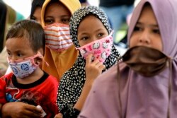 Perempuan dan anak-anak yang memakai masker menunggu pembagian makanan di tengah pandemi virus corona COVID-19 di Blang Bintang, Aceh, pada 6 Mei 2020. (Foto: AFP/Chaideer Mahyuddin)