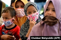 Perempuan dan anak-anak yang memakai masker menunggu pembagian makanan di tengah pandemi virus corona COVID-19 di Blang Bintang, Aceh, pada 6 Mei 2020. (Foto: AFP/Chaideer Mahyuddin)