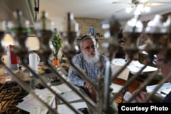 Seen through a menorah is Aaron Goldsmith, a Jewish community leader and business owner in Postville, Iowa. (Credit: Deepak Dophal)