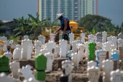 Seorang pekerja menyiram makam-makam baru korban virus corona (Covid-19) di pemakaman Keputih, Surabaya, Jawa Timur. (Foto: AFP) Jawa Timur merupakan provinsi dengan korban meninggal akibat Covid-19 tertinggi.