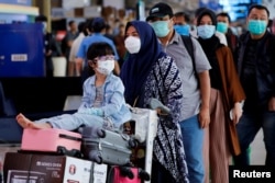 Seorang anak perempuan mengenakan masker bersama ibunya antre untuk pemeriksaan suhu tubuh di tengah penyebaran COVID-19 di Bandara Halim Perdanakusuma, Jakarta, 20 Maret 2020. (Foto: Reuters)
