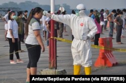 Ilustrasi - Seorang petugas yang mengenakan APD memeriksa suhu pekerja migran Indonesia yang tiba dari Malaysia selama karantina untuk mencegah penyebaran COVID-19, di pangkalan udara Soewondo, Medan, Sumatra Utara, 11 April 2020.