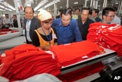 In this file photo taken on Aug. 30, 2017,Prime Minister Hun Sen, center, leans over a garment worker during a visit to a factory outside of Phnom Penh, Cambodia.