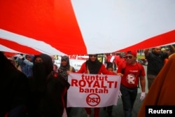 FILE - A protester holds a sign as she walks to Independence Square from Kuala Lumpur Convention Centre (KLCC), during a protest against the Goods and Services Tax (GST), in Kuala Lumpur, May 1, 2014.