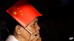 In this photo taken on July 2, 2018, a woman uses a Chinese national flag to protect herself from the sun as she listens to PM Hun Sen who delivering his speech during an inauguration ceremony of a sky bridge in Phnom Penh, Cambodia.