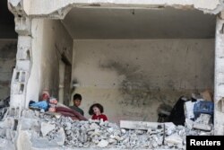 Anak-anak Palestina berdiri di sebuah rumah yang hancur akibat serangan Israel, di tengah konflik yang sedang berlangsung antara Israel dan Hamas, di Rafah, Jalur Gaza selatan, 22 Mei 2024. (Foto: REUTERS/Hatem Khaled)