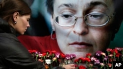 Seorang perempuan tampak meletakkan bunga di depan foto jurnalis Anna Politkovskaya, di Moskow, pada 7 Oktober 2009. Politkovskaya tewas dibunuh karena liputannya yang kritis terhadap Kremlin. (Foto: AP/Pavel Golovkin)