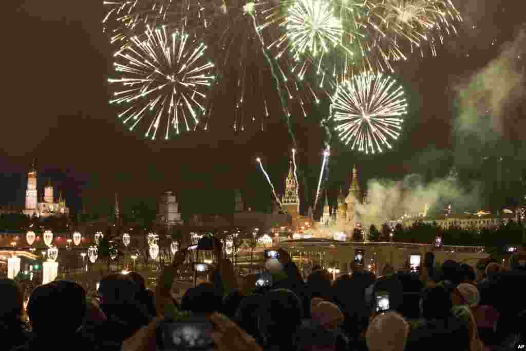 People take pictures as fireworks explode over the Kremlin, during New Year's celebrations in Moscow, Russia, Jan. 1, 2018.