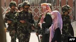 Perempuan etnis Muslim Uighur melewati polisi paramiliter China yang sedang berpatroli di sebuah jalan di Urumqi, ibu kota wilayah Xinjiang China pada 3 Juli 2010. (Foto: AFP)