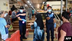 Petugas keamanan memeriksa suhu pengunjung pasar, sambil menjaga jarak sosial, di Penang, Malaysia di tengah pandemi Covid-19, 29 Mei 2020. (Foto: GOH Chai Hin / AFP)
