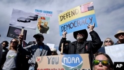 Manifestan Susie House, devan, ak David Hill kenbe pankat pandan y ap pwoteste ak plizye santen lot moun devan kanpis Administrasyon Nasyonal Oseyan ak Atmosfe a nan Boulder, Kolorado, 3 Mas, 2025. 